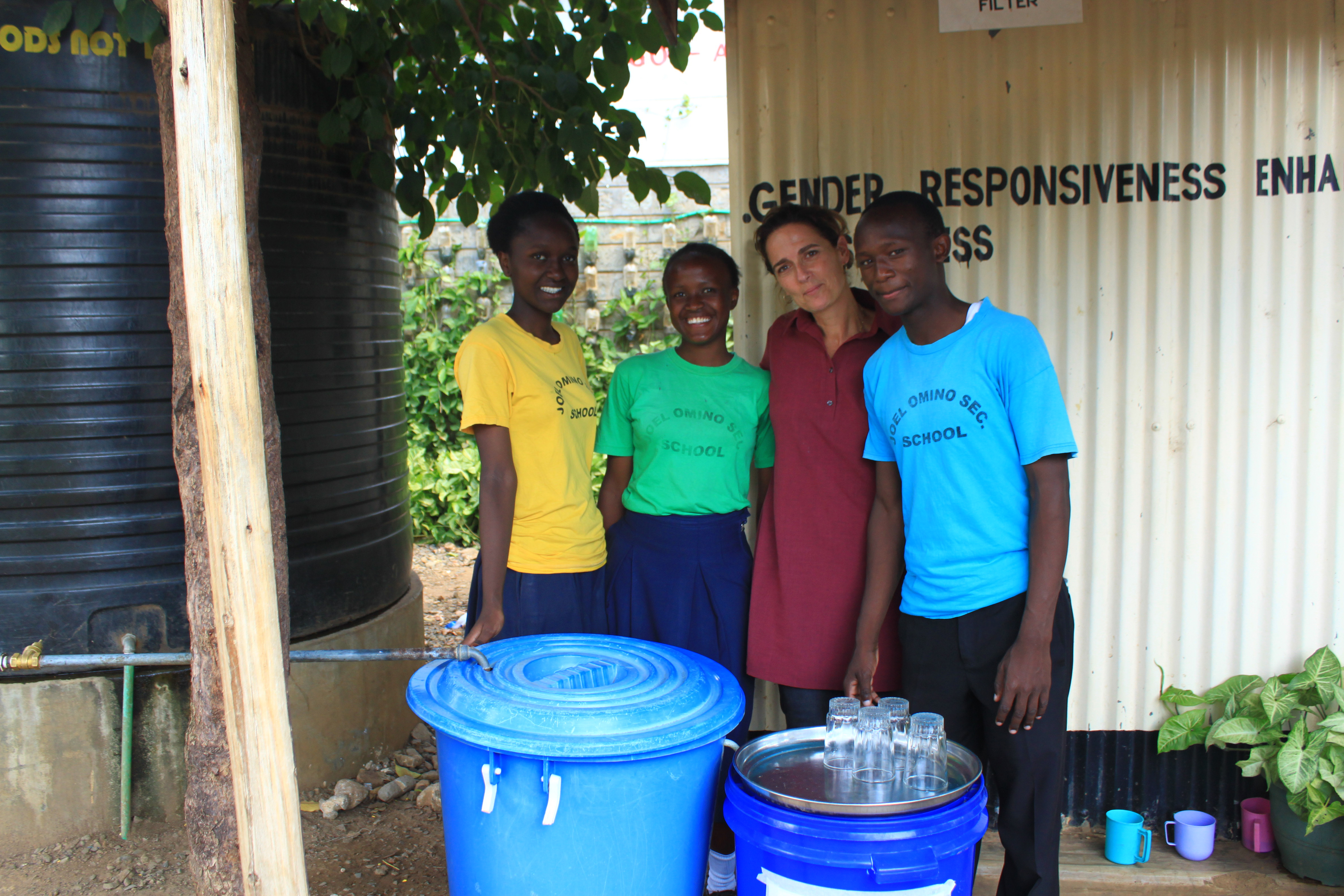 תמונה 1- מיכל עם תלמידים, לצד מערכת סינון החול (bio sand) שהקימו בבית ספרם ג'ואל אומינו בקיסומו קניה.